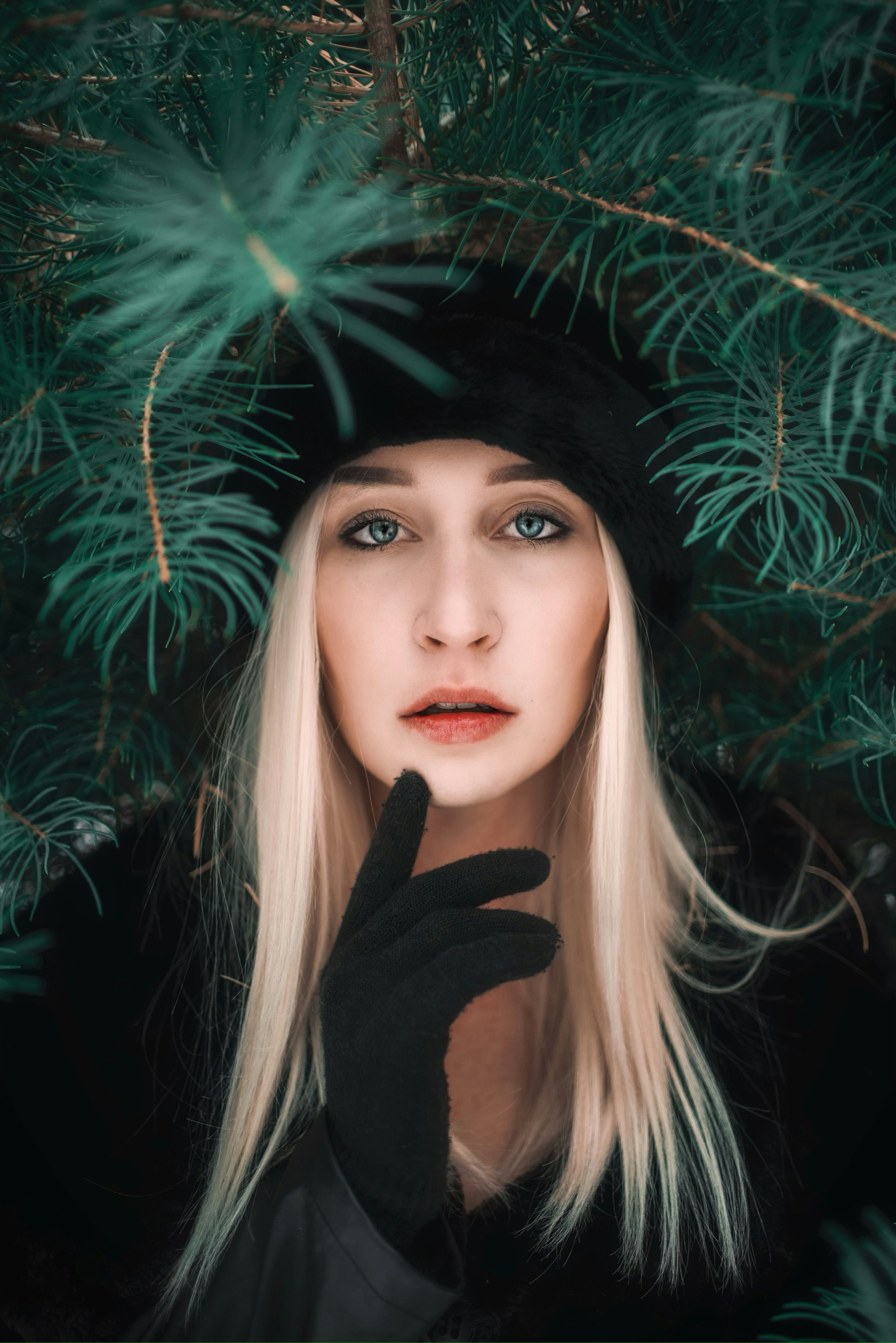 Visage d'une femme blonde portant un bonnet noir et entourée de branches de sapin